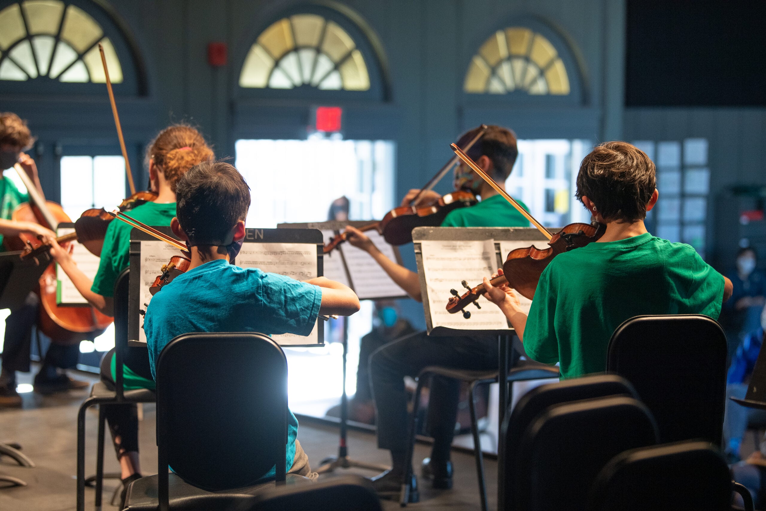 Orchestra group rehearsing with violins on stage.