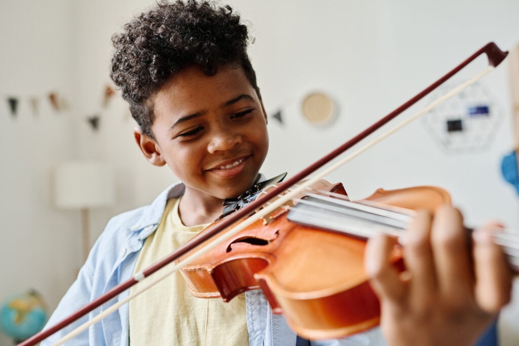 Child playing violin, smiling indoors.