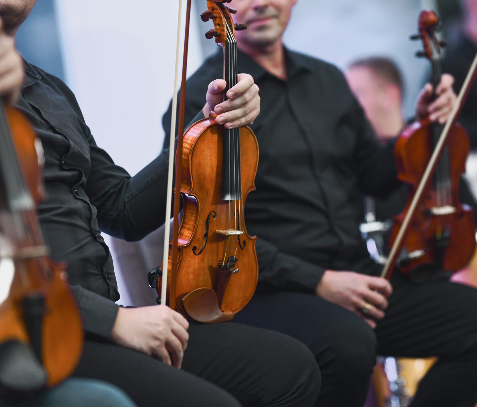 Musicians holding violins in orchestra setting.