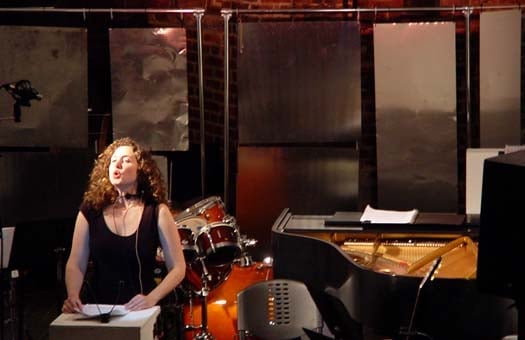 Singer performs on stage with piano and drum set.