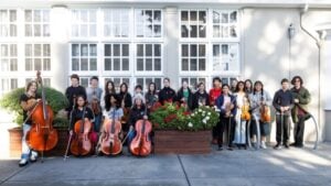 Group of students with musical instruments outside building.