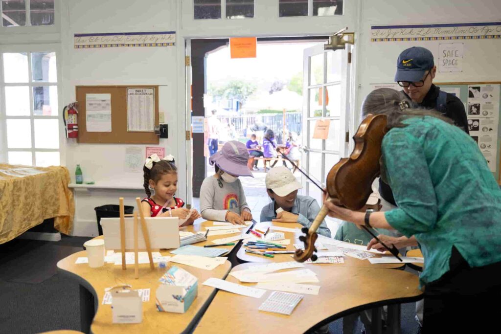 Children crafting at a table with a musician.