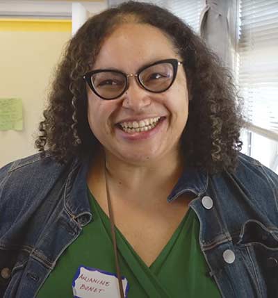 Smiling person wearing glasses and denim jacket indoors.