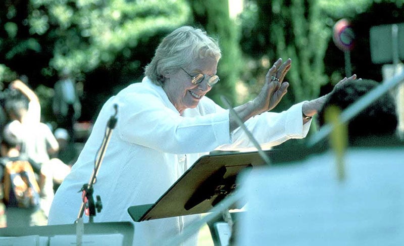 Conductor leading outdoor orchestra performance.