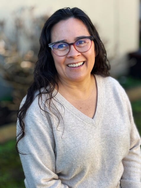 Smiling person with glasses outdoors in sweater.