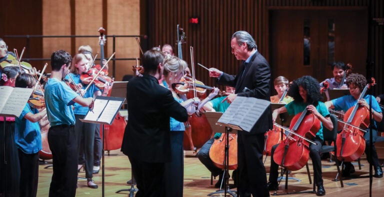 Conductor leads orchestra in performance with musicians playing.
