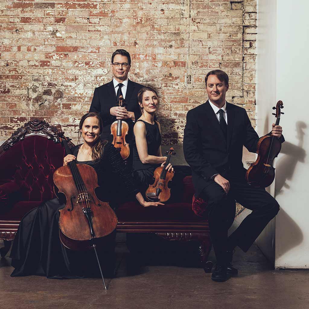 String quartet posing with instruments against brick wall