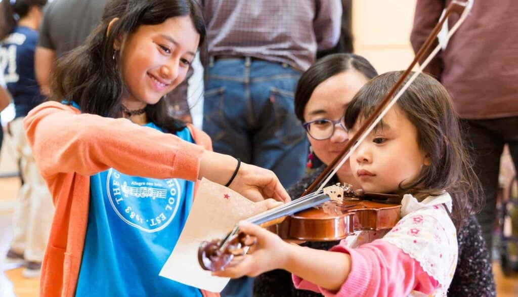 Young girl learning to play violin with teacher.