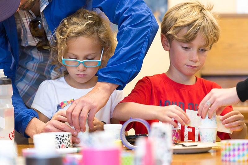Children crafting with adult assistance at table.