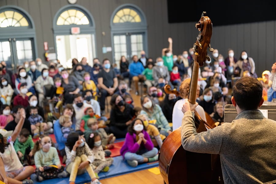 Musicians performing for seated audience in masks, indoors.