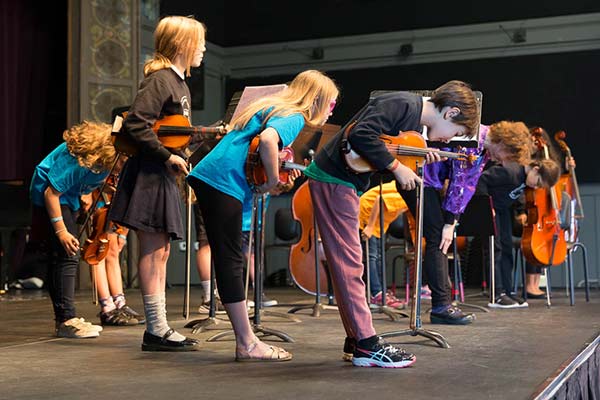 Children performing music with violins on stage.