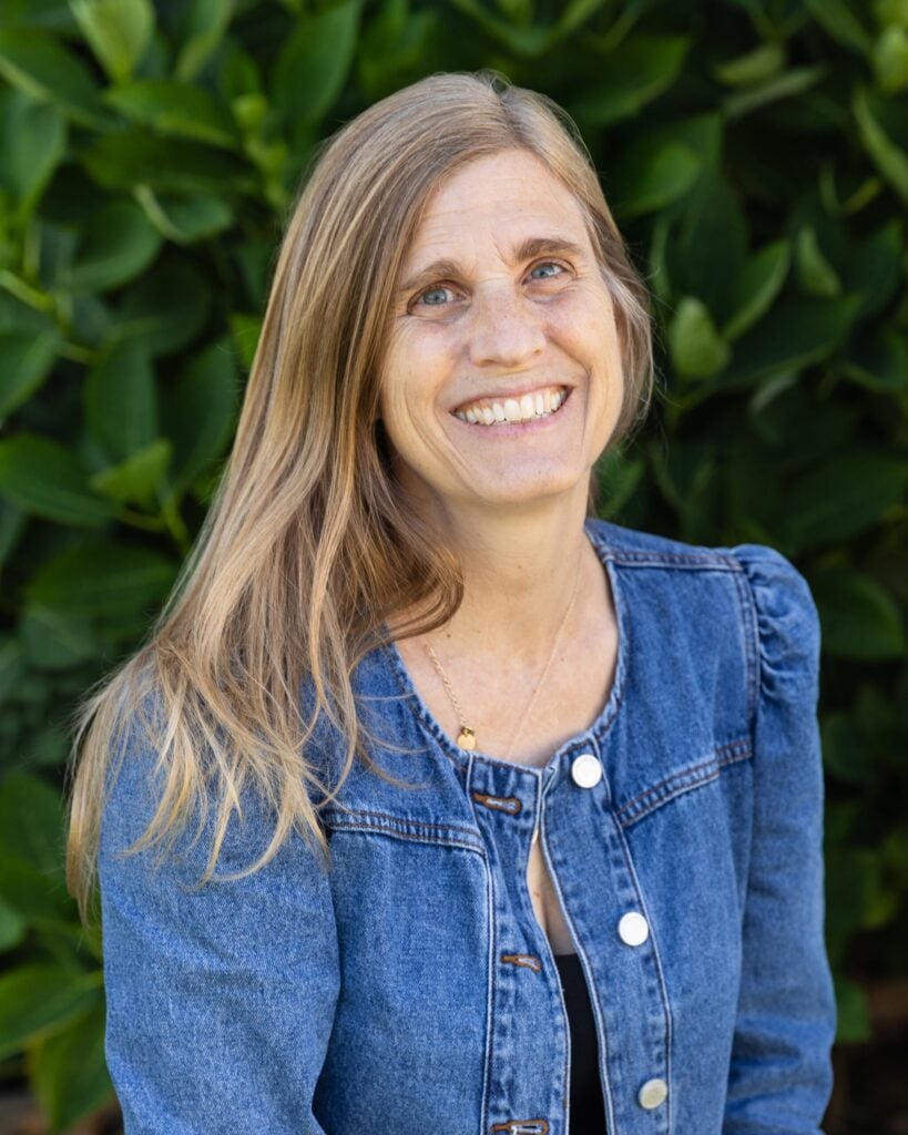 Smiling woman in denim jacket outdoors.