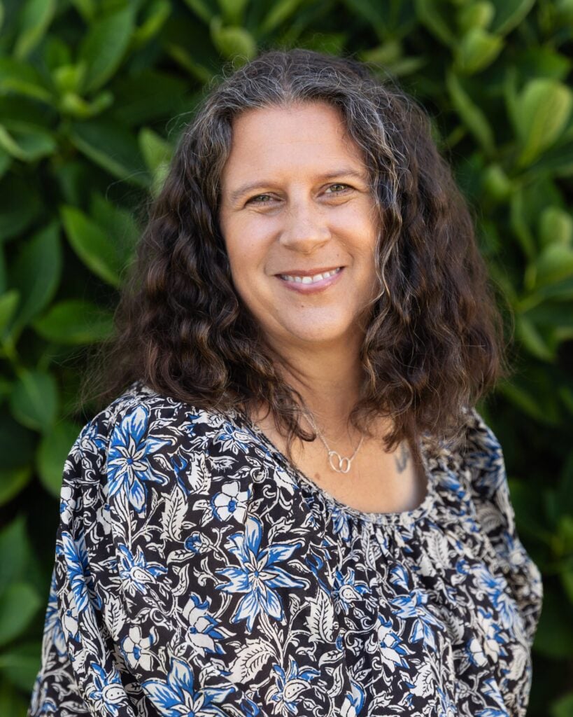 Smiling person with curly hair, wearing floral blouse.