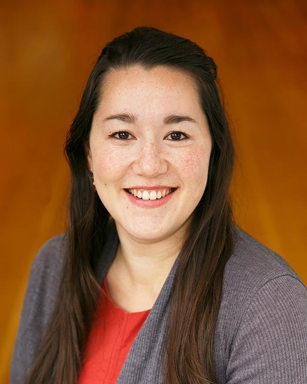 Smiling person with dark hair and gray sweater.