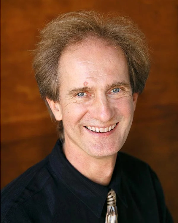 Smiling person with light hair against wooden background.