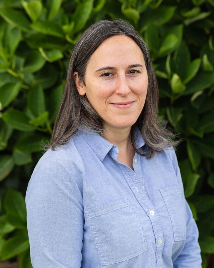 Person smiling in front of green leaves.