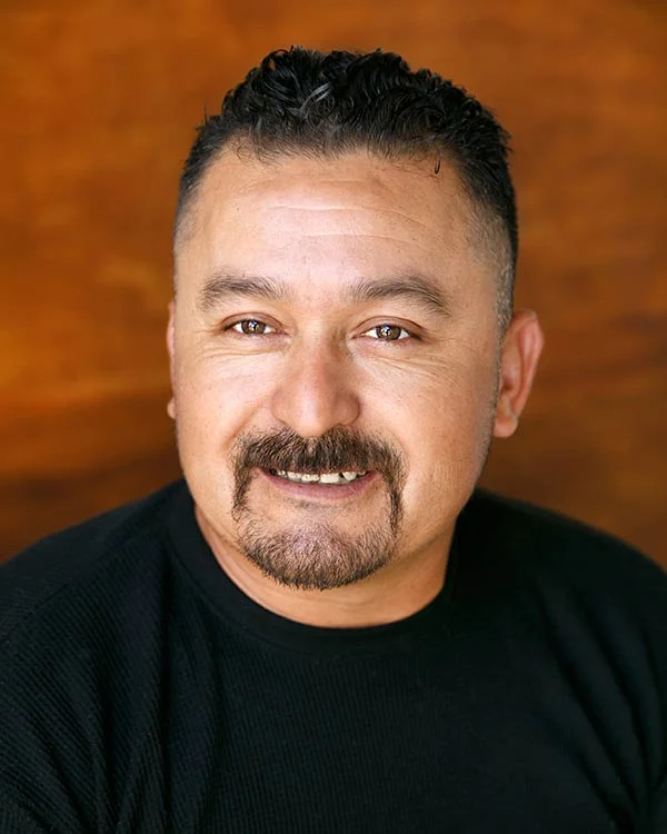 Smiling man with mustache and beard against brown background.