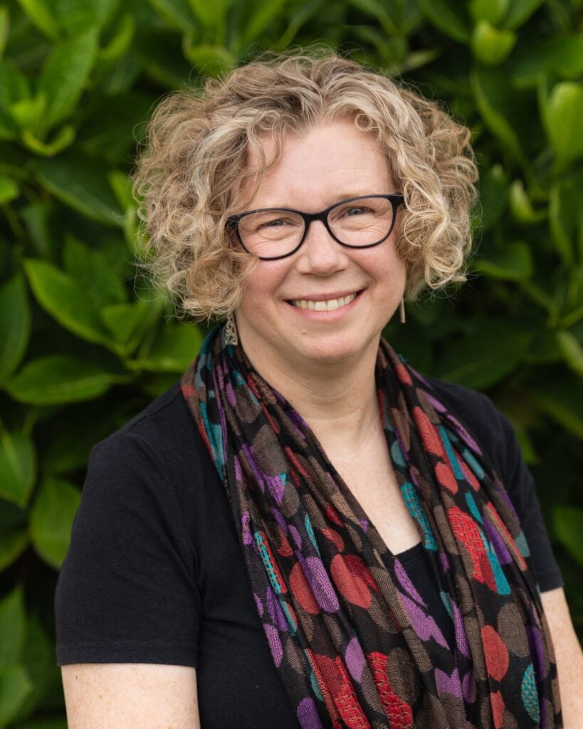 Smiling woman with curly hair and glasses.
