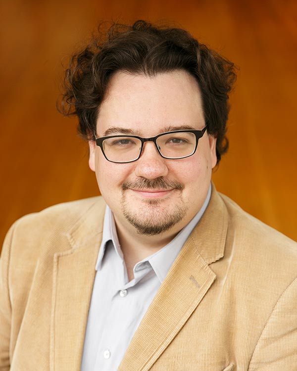 Smiling man in beige blazer and glasses.