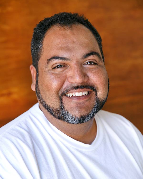 Smiling man in white shirt, brown background.