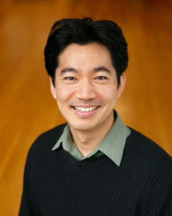 Smiling person in black sweater and green shirt.