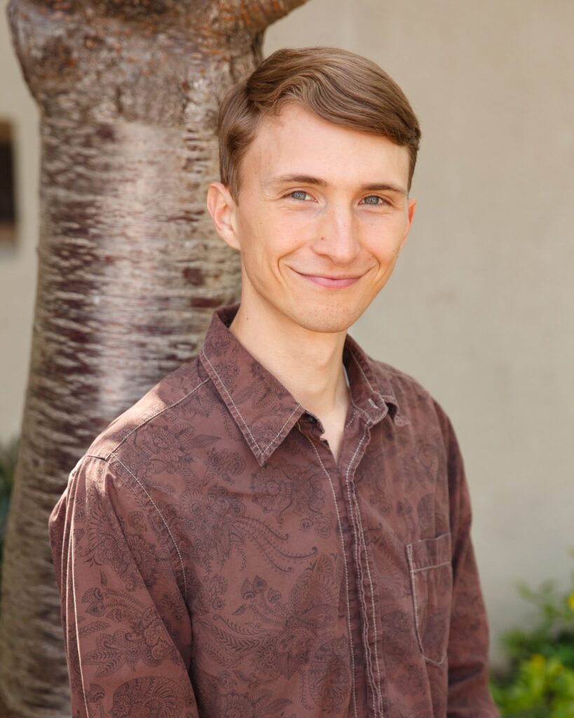 Person smiling in brown patterned shirt outside.