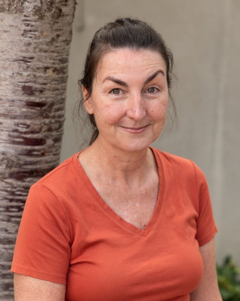 Smiling woman in orange shirt by tree