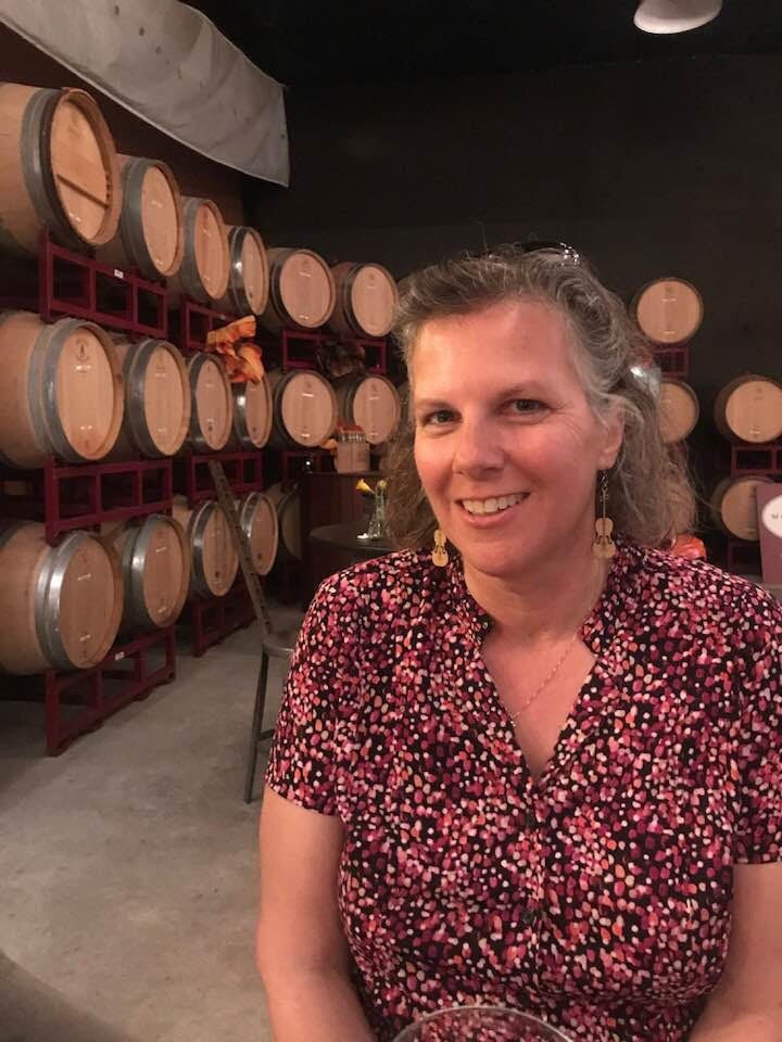 Woman smiling in a winery with barrels.