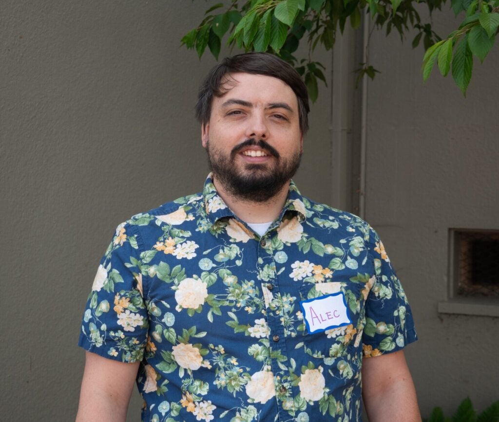 Man in floral shirt with name tag smiling outside.