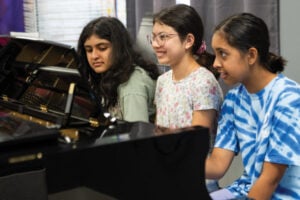 Three girls sitting at a piano, smiling together.