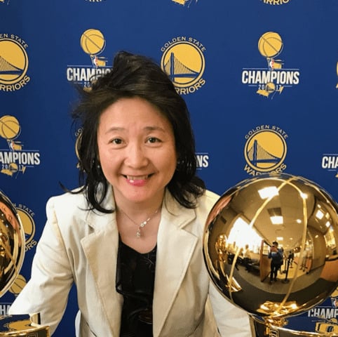 Person smiling with basketball trophies, Golden State Warriors logo.