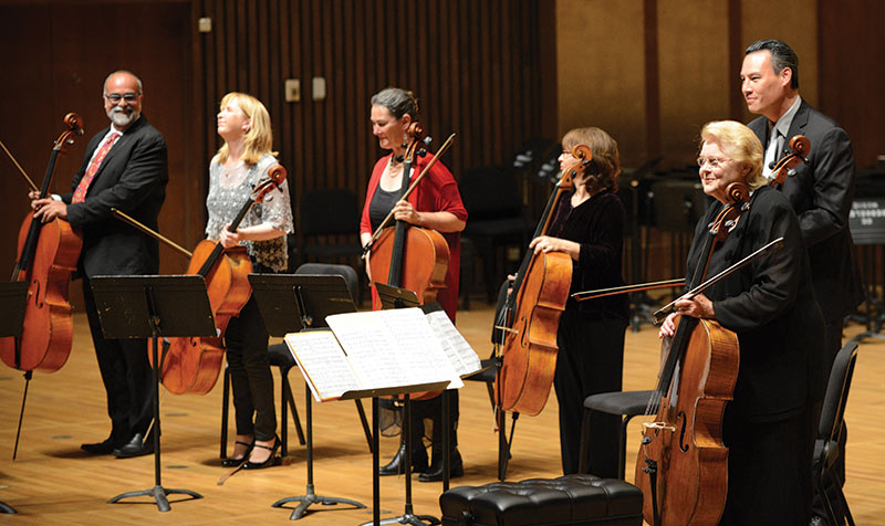 Orchestra musicians with cellos on stage after performance.