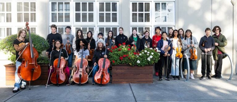 Group of students with string instruments outdoors.