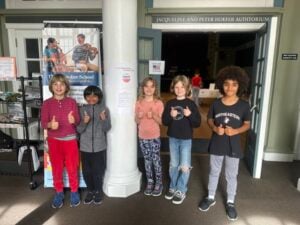 Five kids giving thumbs up in auditorium entrance.