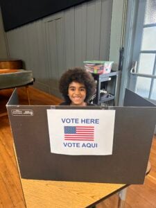 Child at voting booth with USA flag sign.