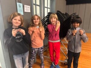 Four kids holding small papers happily indoors.