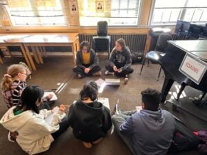 Students in classroom discussion circle on floor.