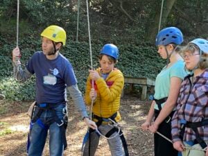 Group learning rock climbing with helmets and ropes.