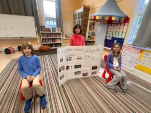 Three children with project display in classroom.