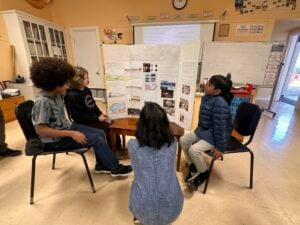 Children discussing volcano project in classroom.