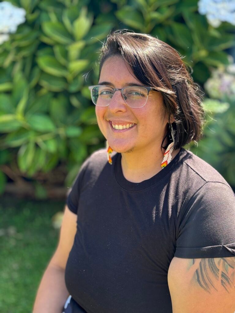 Smiling person with glasses outdoors, black shirt.