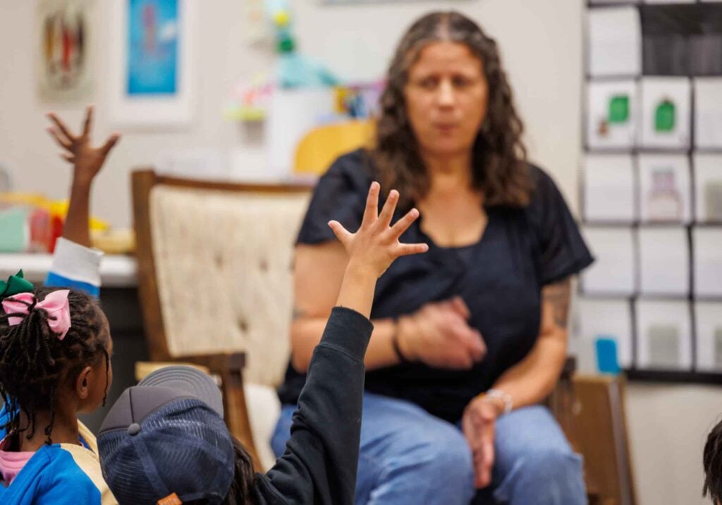 Teacher engaging with children raising hands.