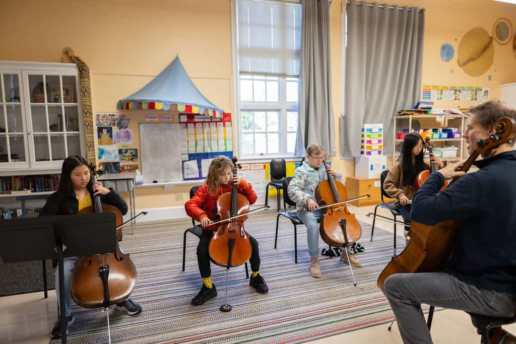 Group of students practicing cello in classroom.