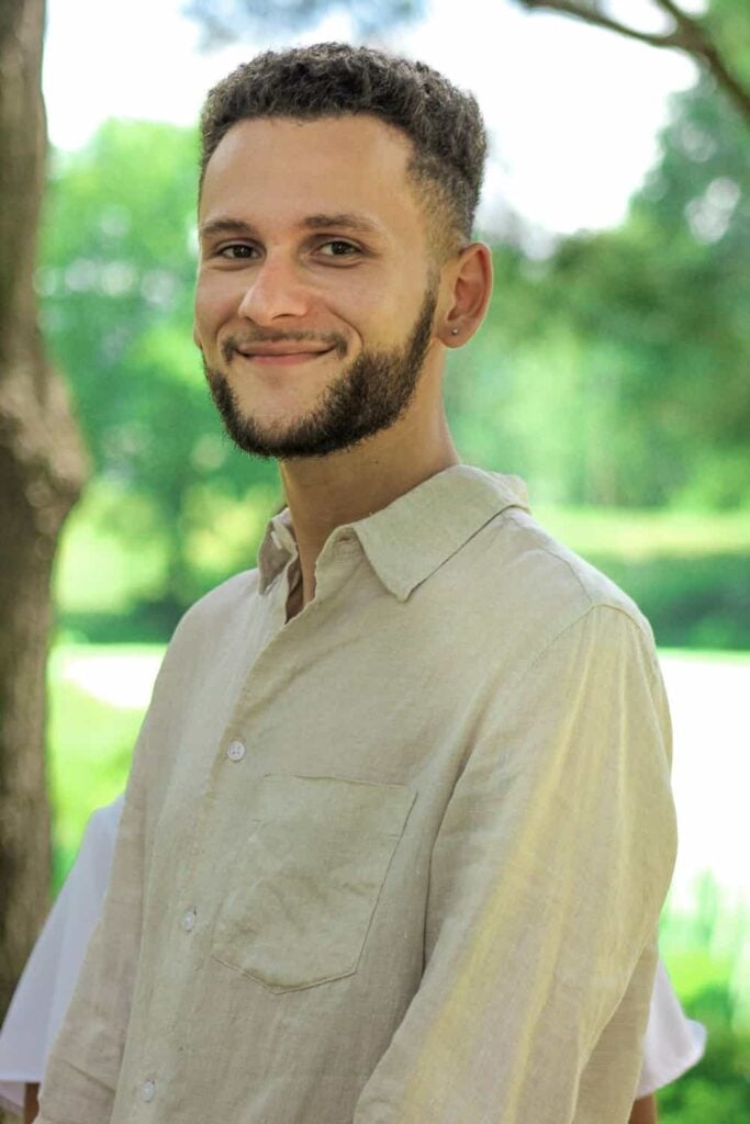 Smiling person outdoors in beige shirt.
