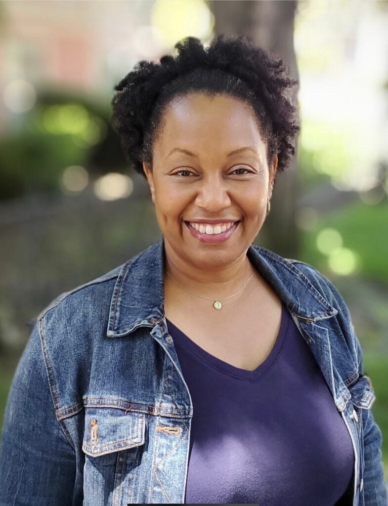 Smiling person in denim jacket outdoors.