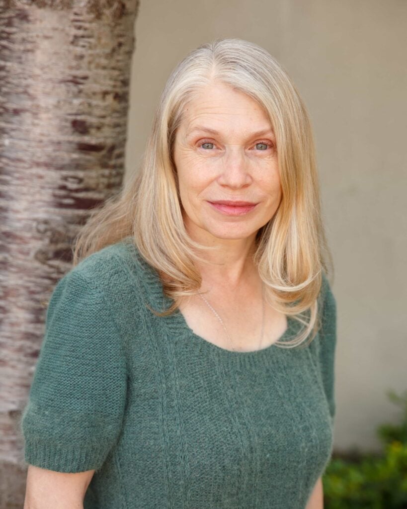 Woman smiling near tree in green sweater.