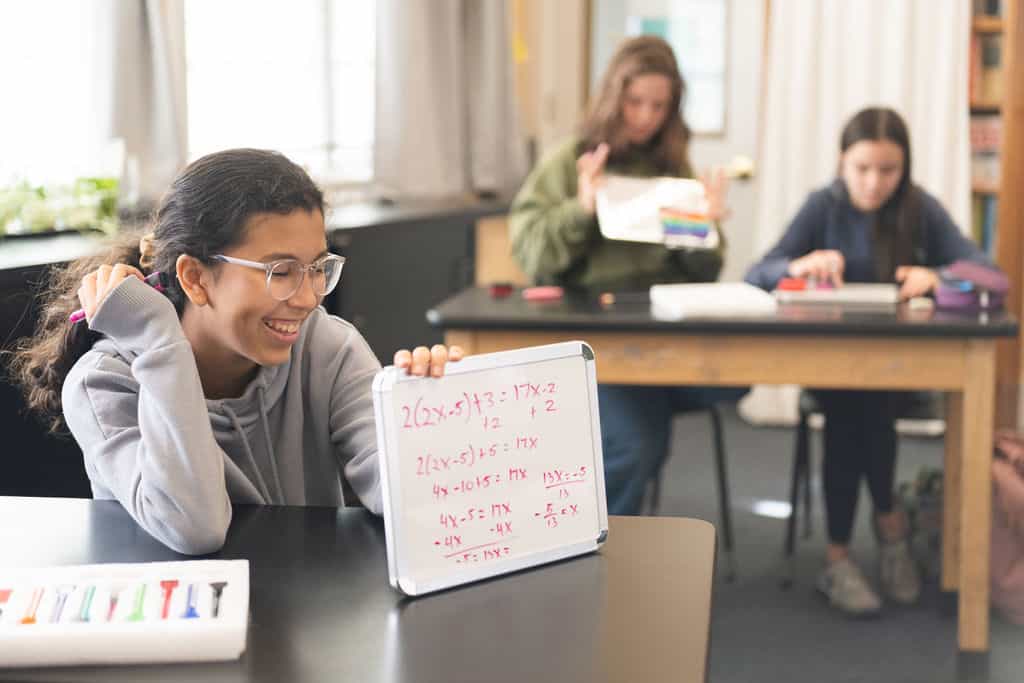 Student solving equations on whiteboard in classroom.