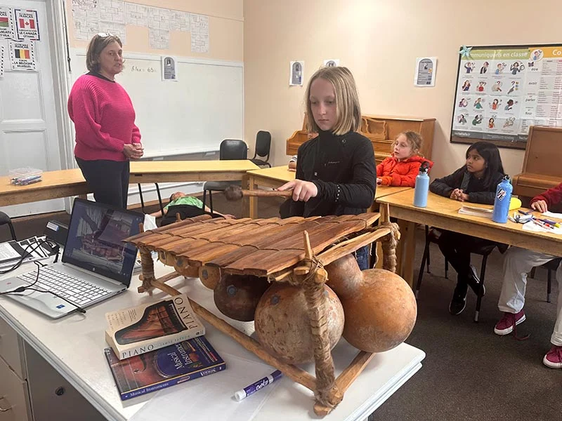 Child plays balafon in classroom setting.