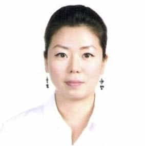 Person wearing white shirt and earrings, neutral expression.