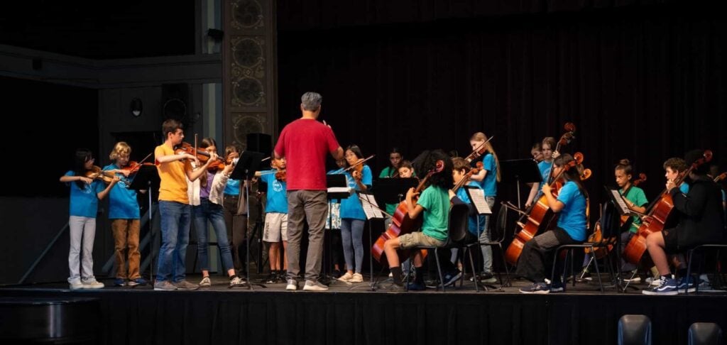 Youth orchestra performing on stage with conductor.